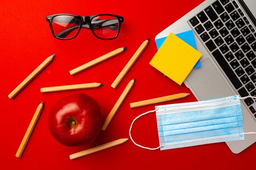 Top view of laptop keyboard, stationery and medical face mask on red background