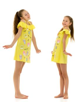 Side View of Barefoot Teen Girls Looking at Each Other Standing on One Leg on Toes, Two Beautiful Sisters Wearing Yellow Short Dresses, Full Length Portrait of Teenagers Isolated on White Background.