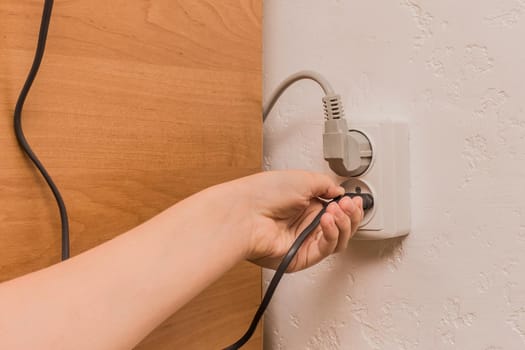 A female hand inserts or removes a plug from an outlet in a modern interior. Safe use of electrical appliances concept.