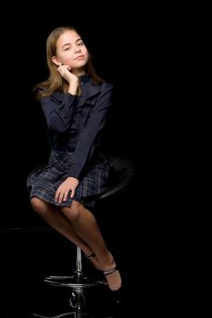 Beautiful Girl Wearing Nice Dress Sitting on Chair Looking to the Side, Front View Portrait of Adorable Girl in Fashionable Stylish Clothes Posing Against Black Background