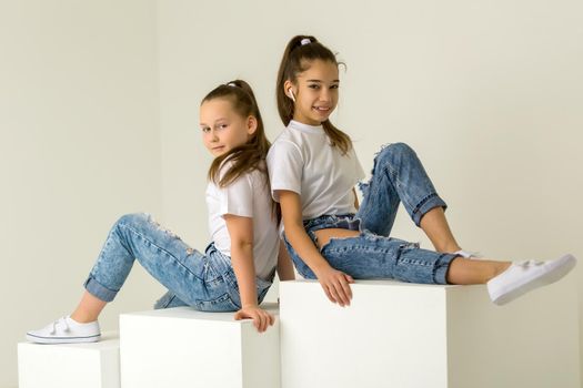 Two little girls posing in the studio on white cubes. The concept of tenderness and beauty.