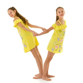 Smiling Teen Girls Standing Back to Back Holding Hands, Barefoot Sisters Wearing in the Same Yellow Dresses Having Fun Together, Full Length Portrait of Cute Teenagers Isolated on White Background.