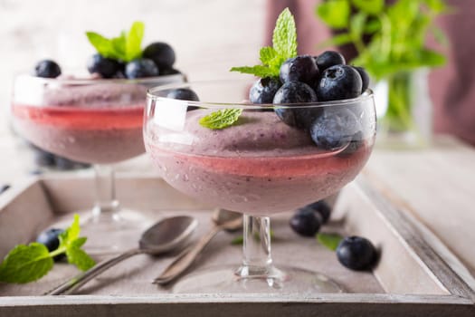 Glass of homemade healthy blueberry dessert with syrup and fresh berries.