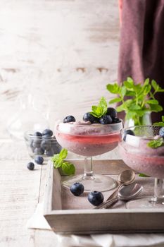 Glass of homemade healthy blueberry dessert with syrup and fresh berries.