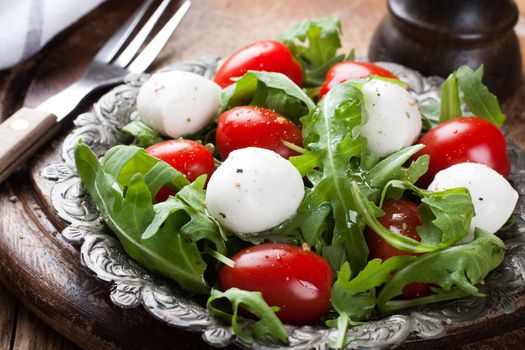 Fresh italian salad with mozzarella cheese, tomato and rucola on vintage old metal plate. Healthy food. Selective focus.