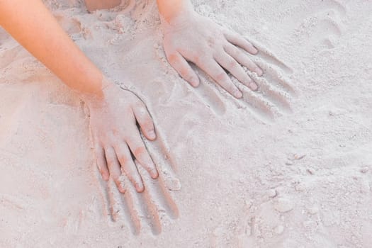 The hands of a young girl lie on a warm white beach sand background.