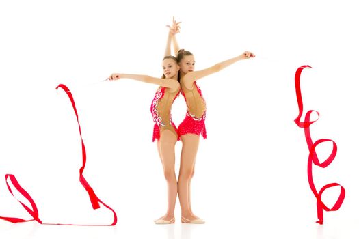 Two charming girls gymnasts, beautiful costumes for the competition, perform synchronized movements with a ribbon. The concept of children's sport, fitness. Isolated on a white background.