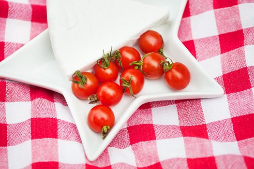 brie cheese and cherry tomatoes on a red tablecloth. close up