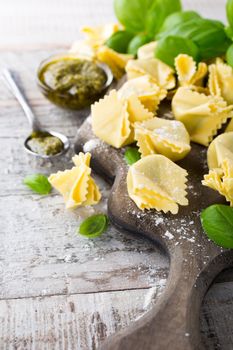 Homemade raw Italian saccottini filled with green pesto on wooden vintage cutting board with basil leaves. Selective focus.