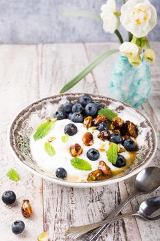 Healthy breakfast, quark with blueberries, pistachios and mint on light wooden background.