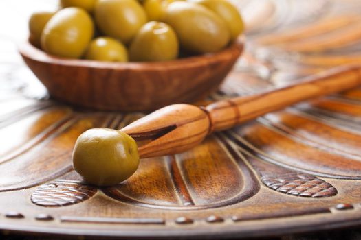 Stick with olive and bowl filled with green olives on a rustic wooden background. Selective focus.