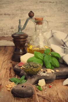 Homemade green pesto in glass bawl on a rustic wooden cutting board and fresh ingredients. Selective focus. Retro style toned.