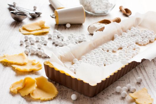 Baking background. Ingredients for dough bottom for tartlet, quiche, tart. Shortbread dough, baking forms, ceramic baking beans, rolling pin. Selective focus.