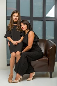 Happy family, mom and daughter near a large panoramic window, in the studio.