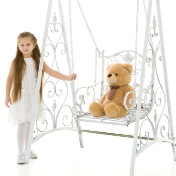 A little girl swings on a swing with a teddy bear. The concept of a happy childhood, the development of a child in the family. Isolated on white background.