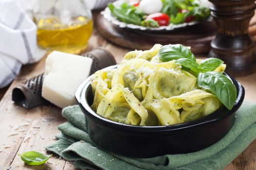 Stuffed Italian tortellini pasta noodles filled with ricotta and spinazi and fresh basil served with pecorino and fresh salad - rucola, cherry tomatoes and mozzarella. Selective focus.