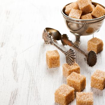 Brown sugar cubes and metal sugat tongs on white wooden background. Selective focus. Background with copy space.