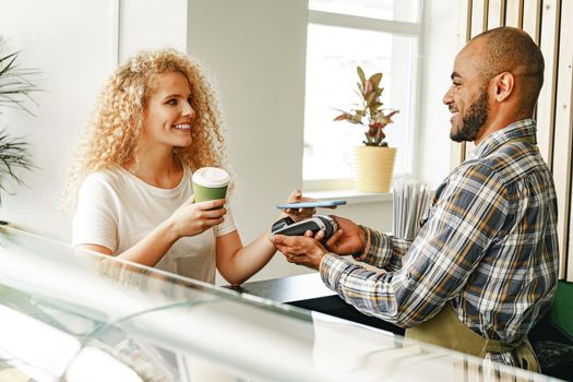 Woman customer of coffee shop paying for coffee through mobile phone using contactless technology close up