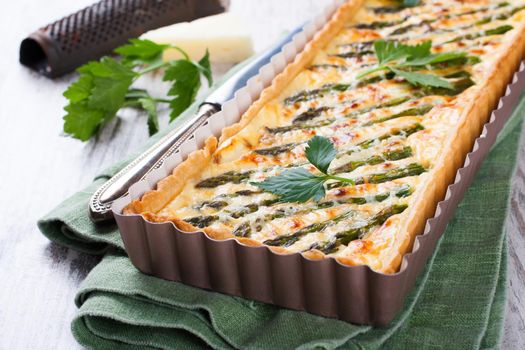 Rectangle-shaped grilled asparagus savory tart with pecorino and bacon next to a french cutting knife on a rustic wooden background