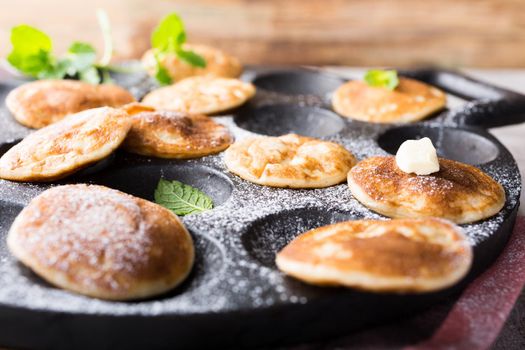 Homemade dutch mini pancakes called poffertjes with mint on special pan with grooves. Healthy food concept with copy space.