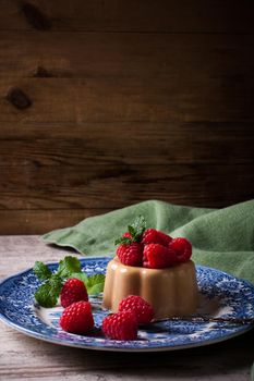 Italian dessert coffee panna cotta served on a blue plate with raspberries and fresh mint on vintage wooden bckground. Selective focus. Retro style toned.