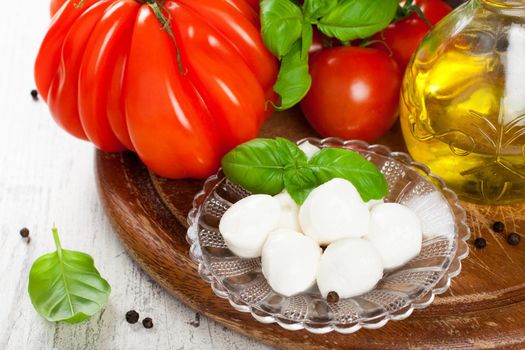 Italian food background with mozzarella balls, tomatoes, basil, olive oil on vintage wooden cutting board. Healthy food concept.