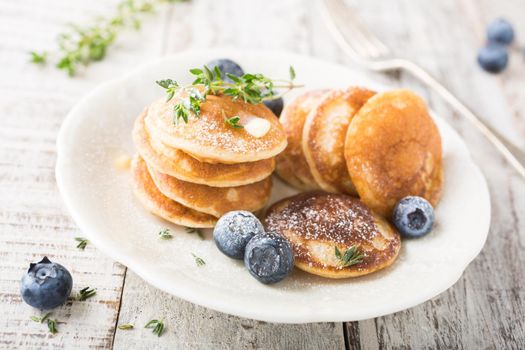 Dutch mini pancakes called poffertjes with blueberries and thyme, sprinkled with powdered sugar. Healthy food concept.