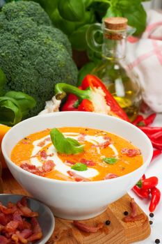 Carrot sweet pepper cream soup with bacon on wooden board