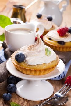 Delicious homemade tartlets served with lemon, lime curd cream, berries and meringue on old cutting board. Selective focus.