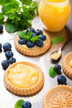 Process of making shortbread tartlet filled with lime curd and blueberries on old vintage metal background. Holiday concept. Selective focus.