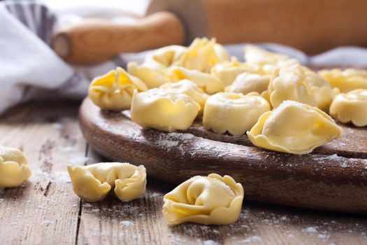 Freshly prepared Italian tortellini on wooden vintage cutting board with a rolling pin. Selective focus.