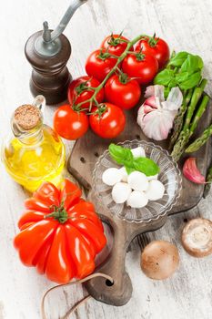 Italian food background, with tomatoes, basil, mushrooms, mozzarella balls, olive oil on vintage wooden cutting board. Healthy food concept.