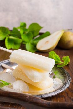 Homemade pear popsicles on metal plate with ice and pears. Summer food concept. With copy space.