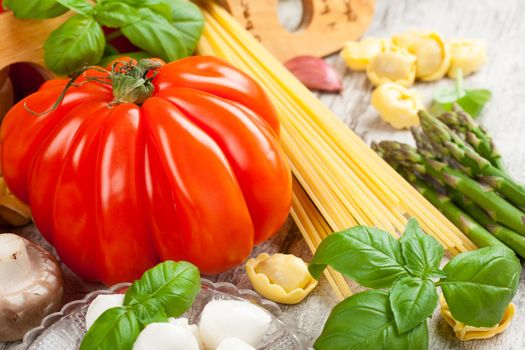 Italian food background, with tomatoes, basil, spaghetti, mushrooms, mozzarella balls, olive oil, spaghetti meter on vintage white wooden table. Healthy food concept.