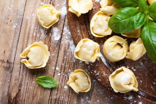 Homemade raw Italian tortellini on wooden vintage cutting board with a rolling pin. Selective focus.