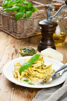 Cooked homemade tagliatelle pasta with green pesto sauce, grated pecorino cheese and basil on white plate on old wooden background.