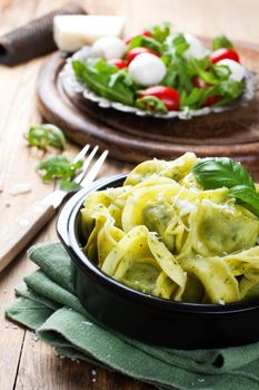 Dish of savory Italian tortellini pasta noodles filled with ricotta and spinazi and fresh basil served with pecorino and fresh salad - rucola, cherry tomatoes and mozzarella. Selective focus.