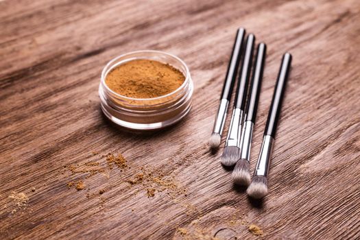 Loose compact mineral powder for face and a brushes for powder and visage on wooden background. Eco friendly and organic cosmetics