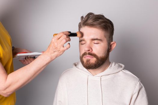 Professional makeup artist doing young man makeup in studio