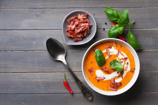 Carrot sweet pepper cream soup with bacon on old wooden background