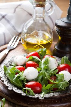 Fresh italian salad with mozzarella cheese, tomato and rucola on vintage old metal plate. Healthy food. Selective focus.