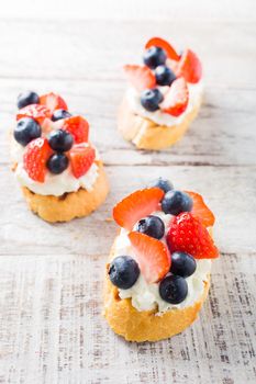 Small canape, crostini with grilled baguette with cream cheese, blueberry, strawberry and mint on old white wooden background. Delicious appetizer or dessert.