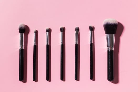 Various make-up brushes on pink background, top view. Cosmetics and beauty