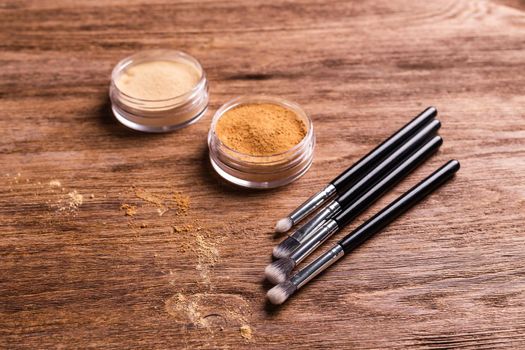 Loose compact mineral powder for face and a brushes for powder and visage on wooden background. Eco friendly and organic cosmetics