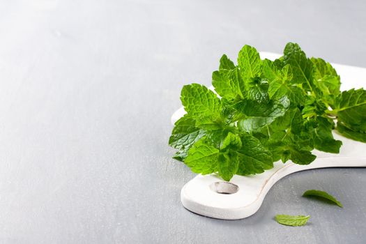 Fresh mint on white cutting board on gray background. Selective focus. Background with copy space.