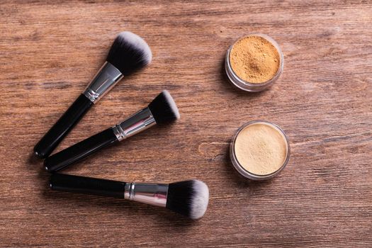 Loose compact mineral powder for face and a brushes for powder and visage on wooden background. Eco friendly and organic cosmetics