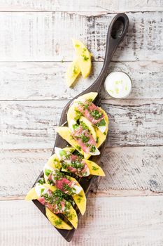 Rolls of mozzarella, basil and Parma ham on slices of mango with yoghurt sauce on wooden cutting board. Healthy eating concept with copy space