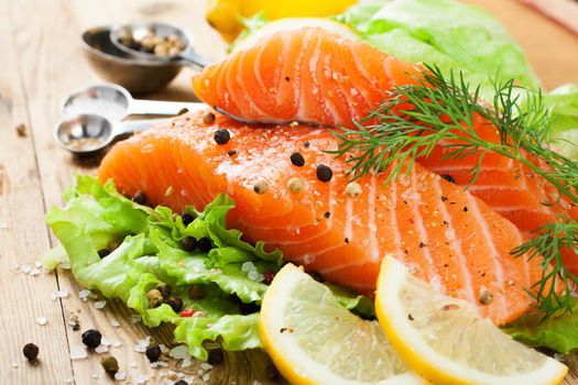 Delicious salmon fillet, rich in omega 3 oil, aromatic spices and lemon on fresh lettuce leaves on rustic wooden background. Healthy food, diet and cooking concept.