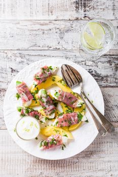 Rolls of mozzarella, basil and Parma ham on slices of mango with yoghurt sauce on white plate. Healthy eating concept with copy space