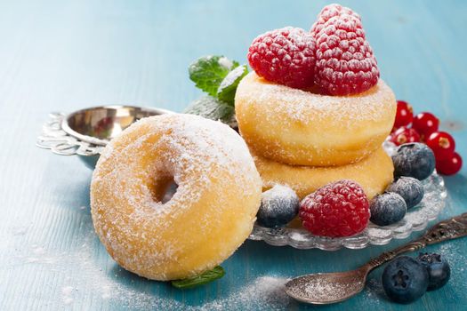 Morning breakfast with mini donuts and berries on plate under powdered sugar on blue wooden background. Tasty donuts closeup. Doughnut. Selective focus.